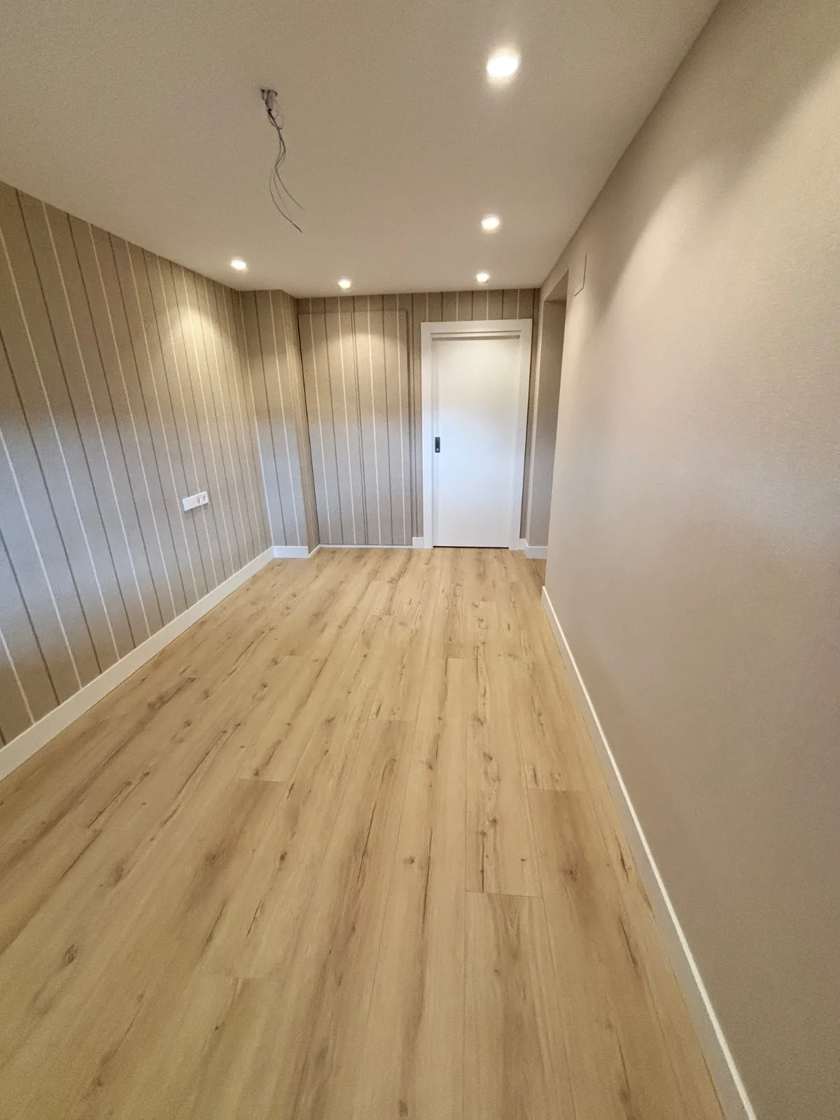Habitación reformada con papel pintado a rayas, suelo laminado y focos empotrados