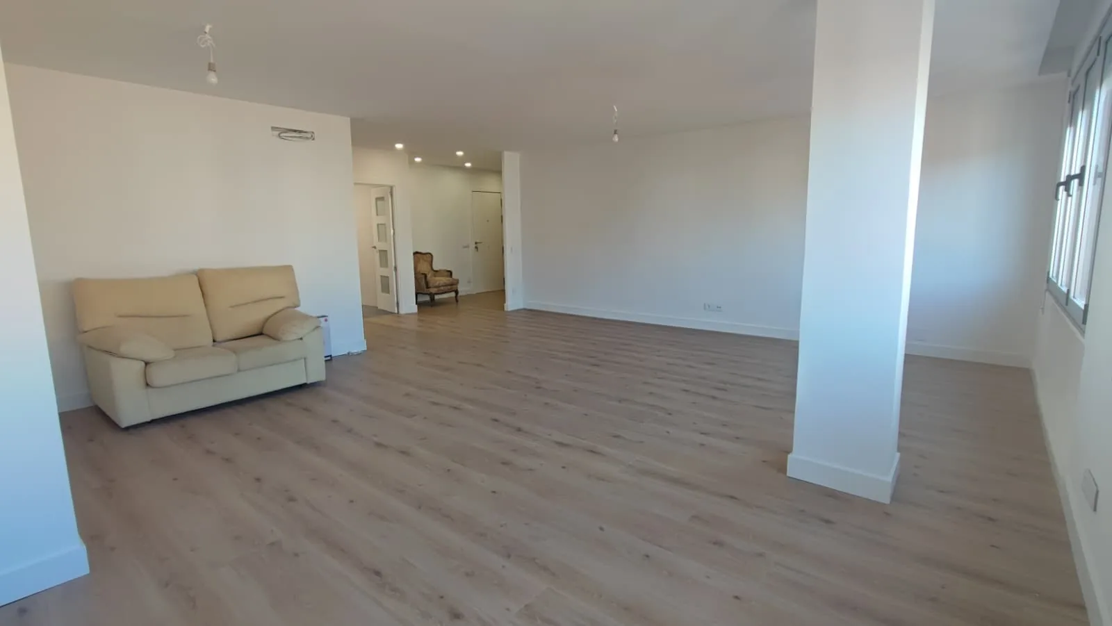 Salón amplio con suelo laminado, pilar y zona de entrada al fondo en piso reformado